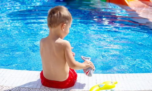 Happy child in the pool playing with a water gun. Recreation