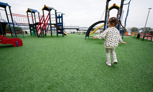 A young child happily runs across a vibrant playground with slides and climbing frames, embodying joy and childhood freedom.